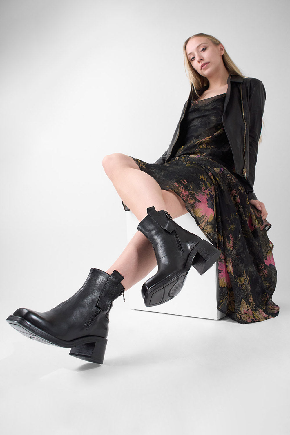 Woman wearing black leather boots and a floral dress on a white background